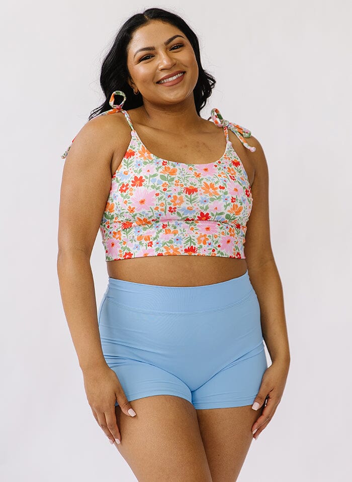 Photo of a woman wearing a floral shoulder-tie swim crop top and a blue swim short bottom