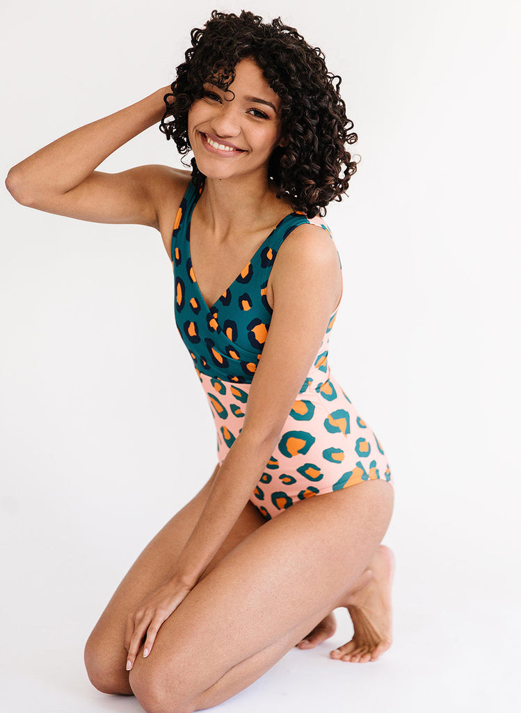 Photo of a woman sitting on her knees wearing a pink and blue leopard print one piece swimsuit