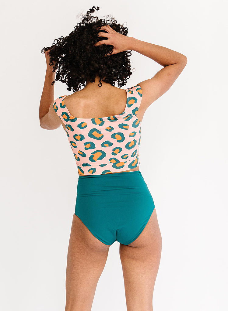 Photo of a woman wearing a peach leopard cap-sleeve swim crop top and a dark green swim bottom- back angle