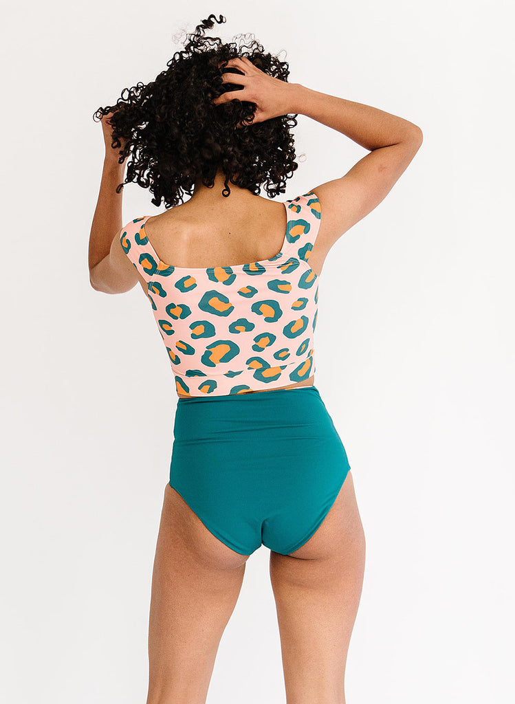 Photo of a woman with her back facing us wearing pink leopard print cropped swim top with blue high waist swim bottoms