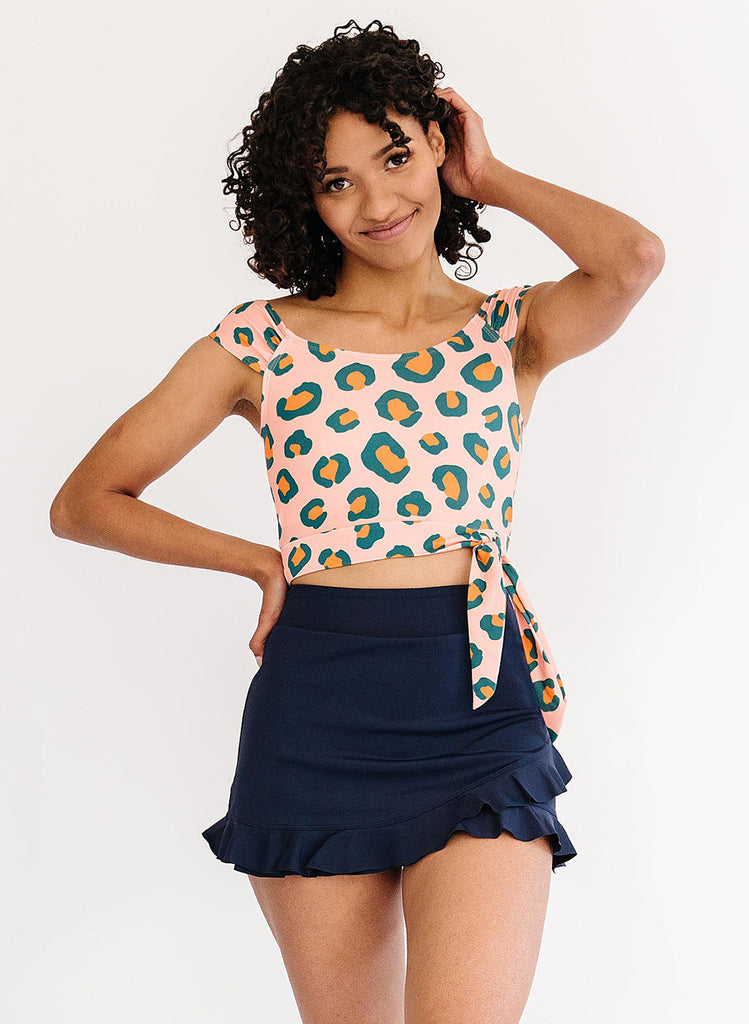 Photo of woman wearing a pink leopard print cropped swim top with a blue swim skirt