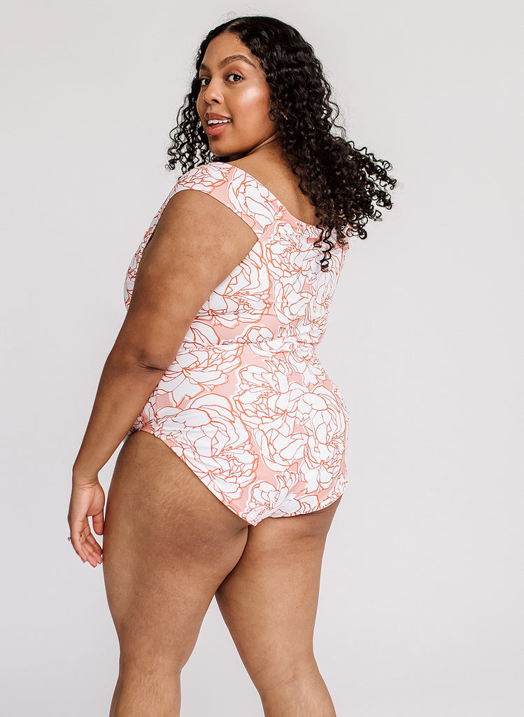 Photo of a woman wearing a pink and white floral cap-sleeved one piece swim suit- back angle