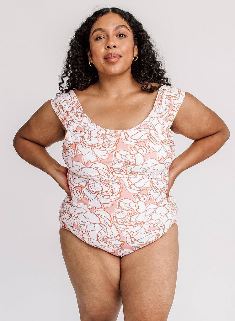 Photo of woman with her hands on her hips while wearing pink and white floral one piece swimsuit