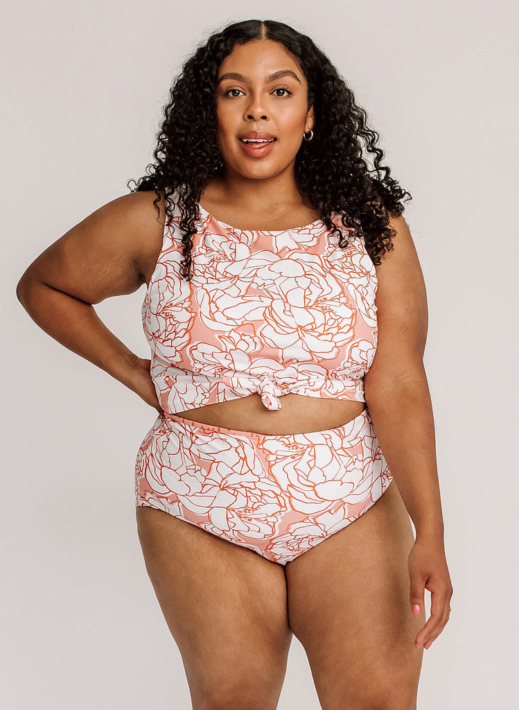 Photo of a woman with her hand on her hip wearing a pink and white floral cropped swim top with pink and white floral high waist swim bottoms