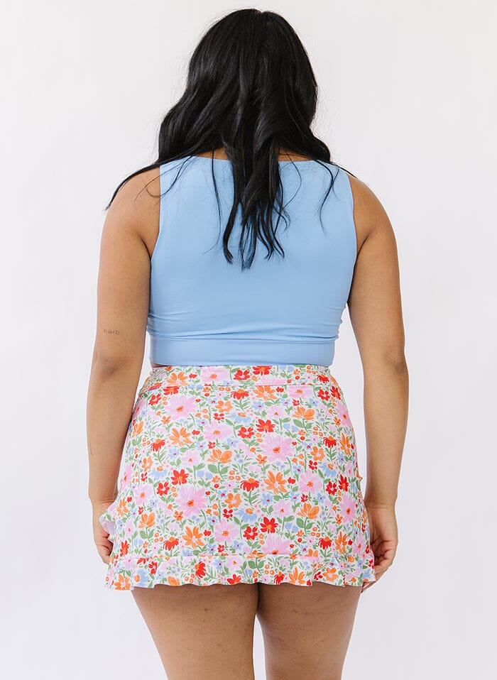 Photo of a woman wearing a floral swim skirt bottom and a blue swim crop top back angle