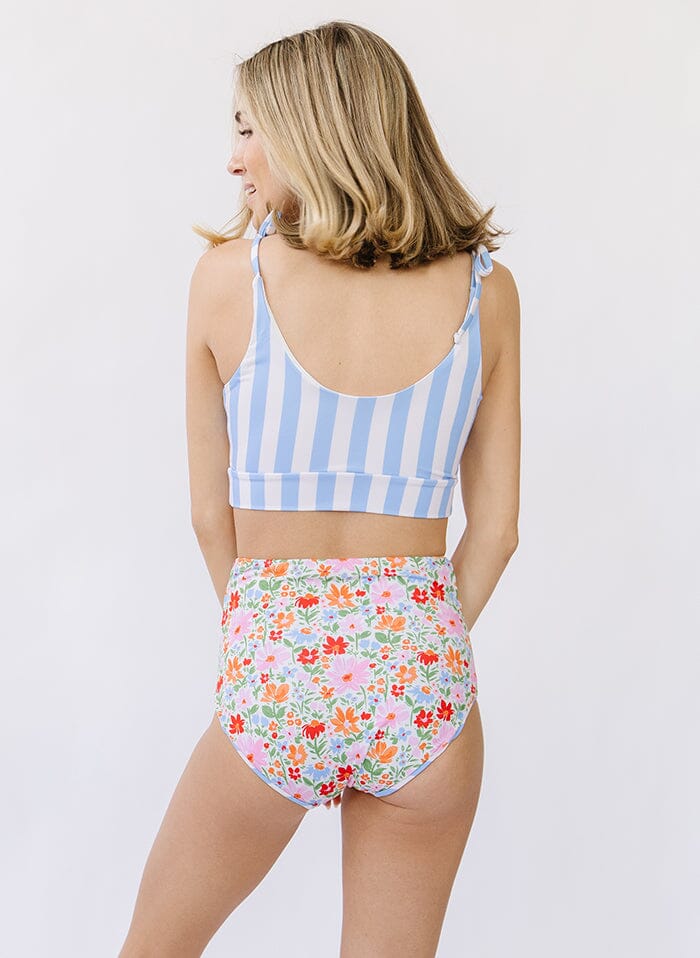 Photo of a woman wearing a peri stripe shoulder-tie swim crop top and a floral swim bottom back angle