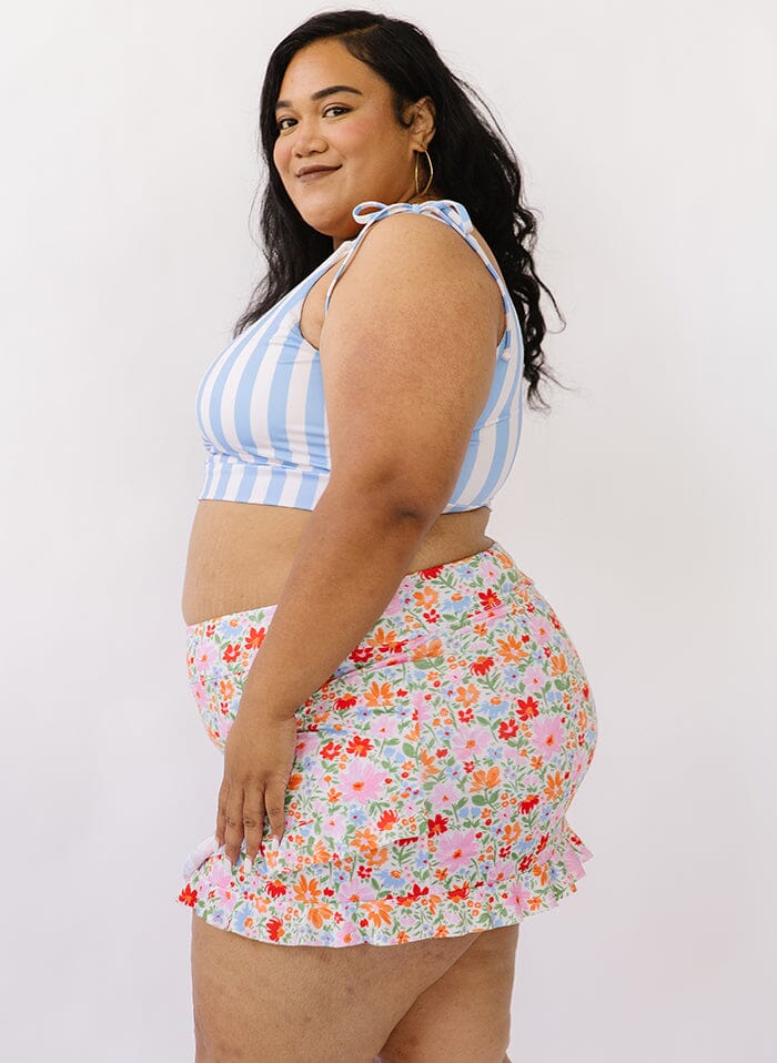 Photo of a woman wearing a peri stripe shoulder-tie swim crop top and a floral swim skirt bottom side angle