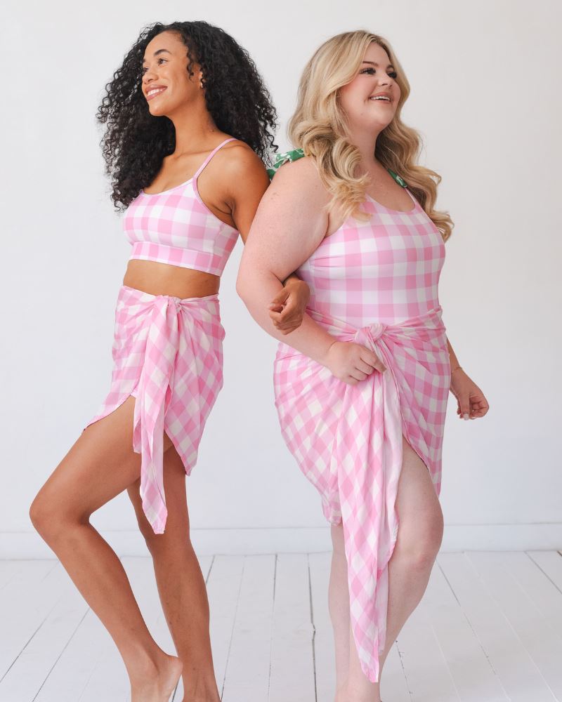 Photo of two women one wearing a pink gingham bralette with a pink gingham sarong the other wearing a pink gingham swim one piece with a pink gingham sarong