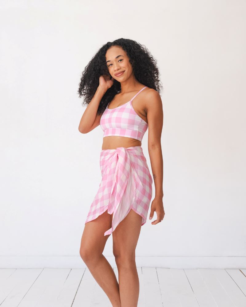 Photo of a woman wearing a pink and white checkered Sarong and a pink and white checkered swim bralette side angle