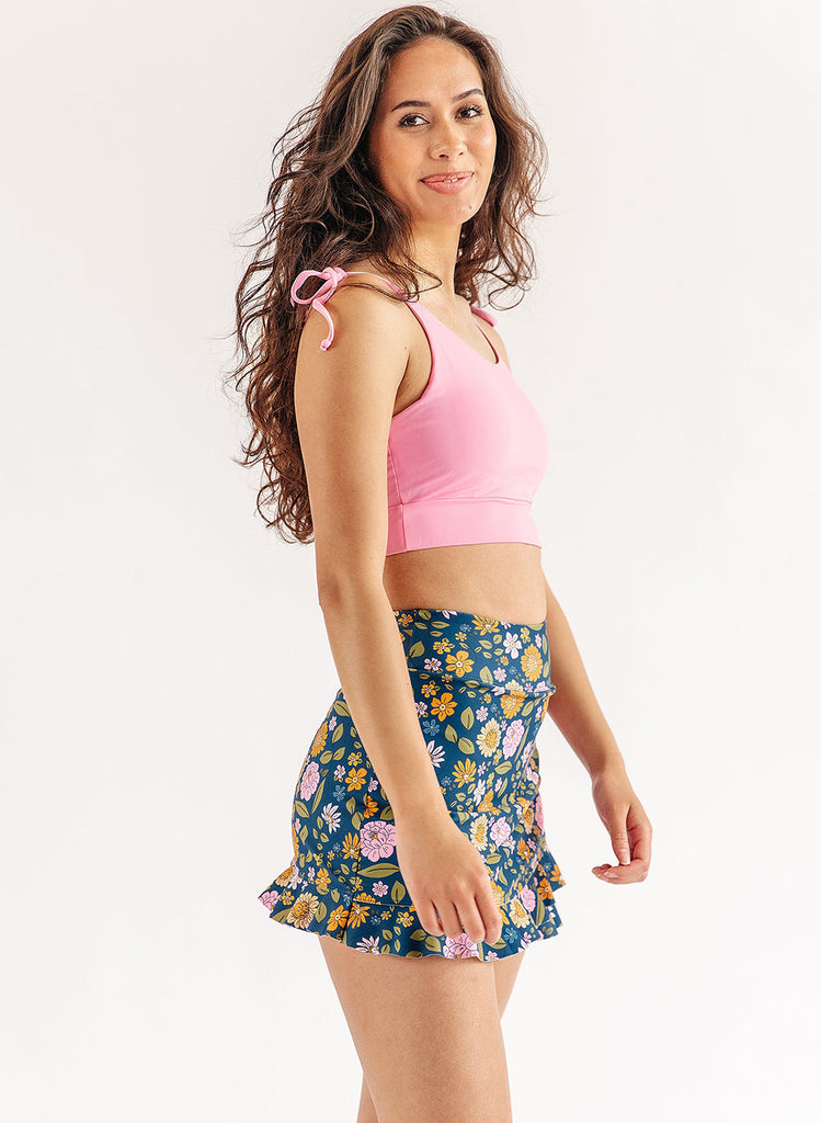 Photo of woman wearing pink cropped swim top and multi color floral swim skirt side angle