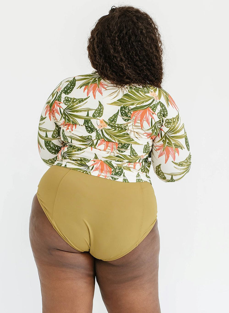 Photo of a woman wearing a tropical floral rash guard swim top and a cactus green swim bottom- back angle