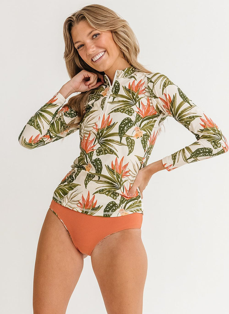 Photo of a woman wearing a green floral long sleeve swim top with orange high waist swim bottoms