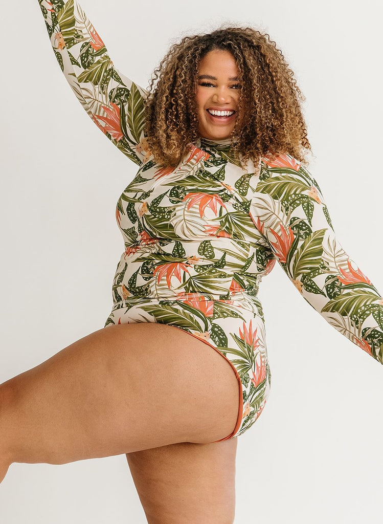 Photo of a woman with her hands in the air wearing a green floral long sleeve swim top with green floral high waist swim bottoms
