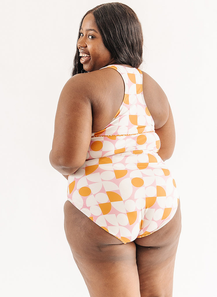 Photo of woman wearing orange and white geometric swim top with orange and white geometric swim bottoms back angle