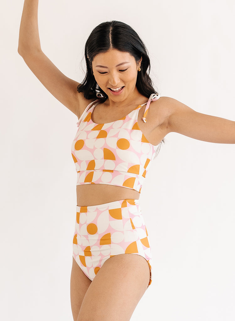 Photo of woman wearing orange and white geometric cropped swim top with orange and white geometric swim bottoms