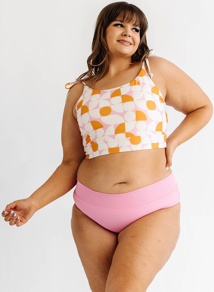 Photo of woman wearing orange and white geometric cropped swim top with pink swim bottoms