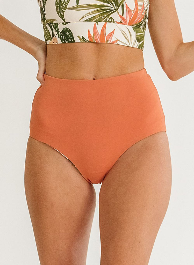 Close up photo of woman wearing a green floral cropped swim top with orange high waist swim bottoms