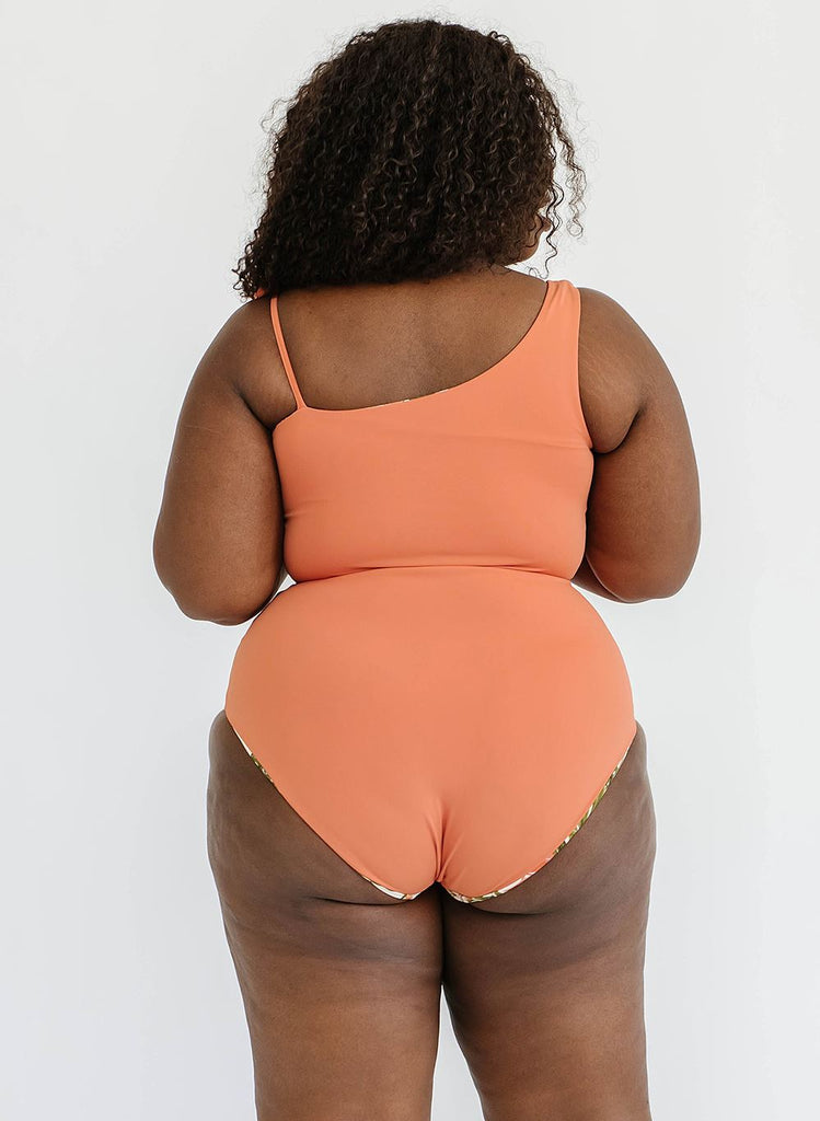 Photo of a woman with her back facing us wearing an orange cropped swim top with orange high waist swim bottoms
