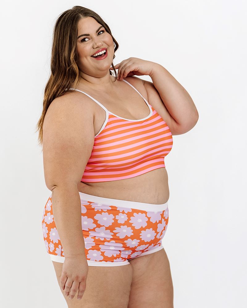 Photo of a woman wearing a Sherbet stripe swim bralette and a Daphne floral swim short bottom side angle