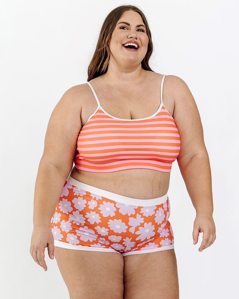 Photo of a woman wearing a Daphne floral retro swim short bottom and a orange and pink stripe swim bralette