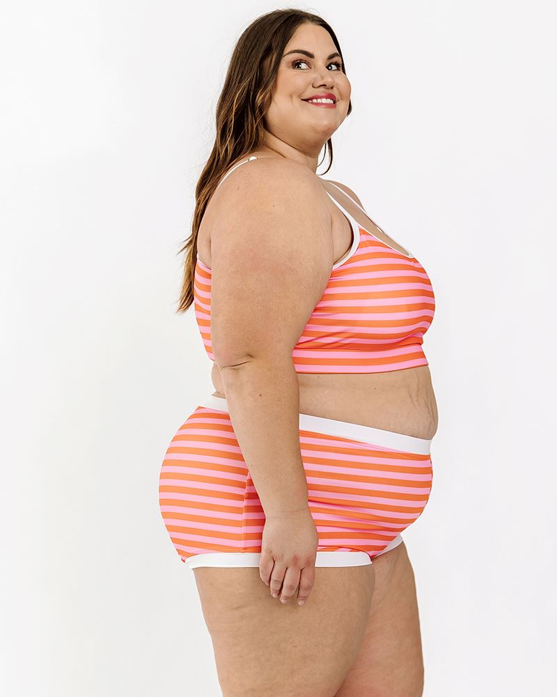 Photo of a woman wearing a Sherbet stripe swim bralette and a sherbet stripe swim short bottom side angle