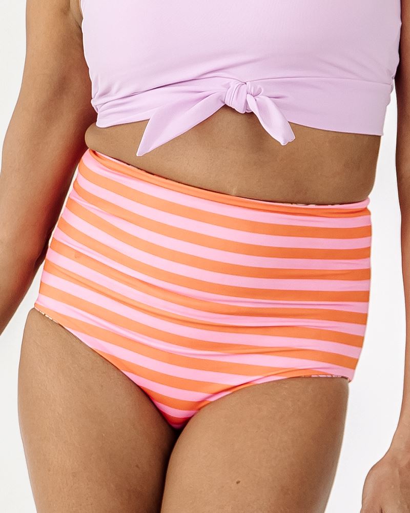 Photo of a woman wearing a Groovy Blooms/sherbet stripe reversible swim bottom stripe side and a Lilac swim crop top