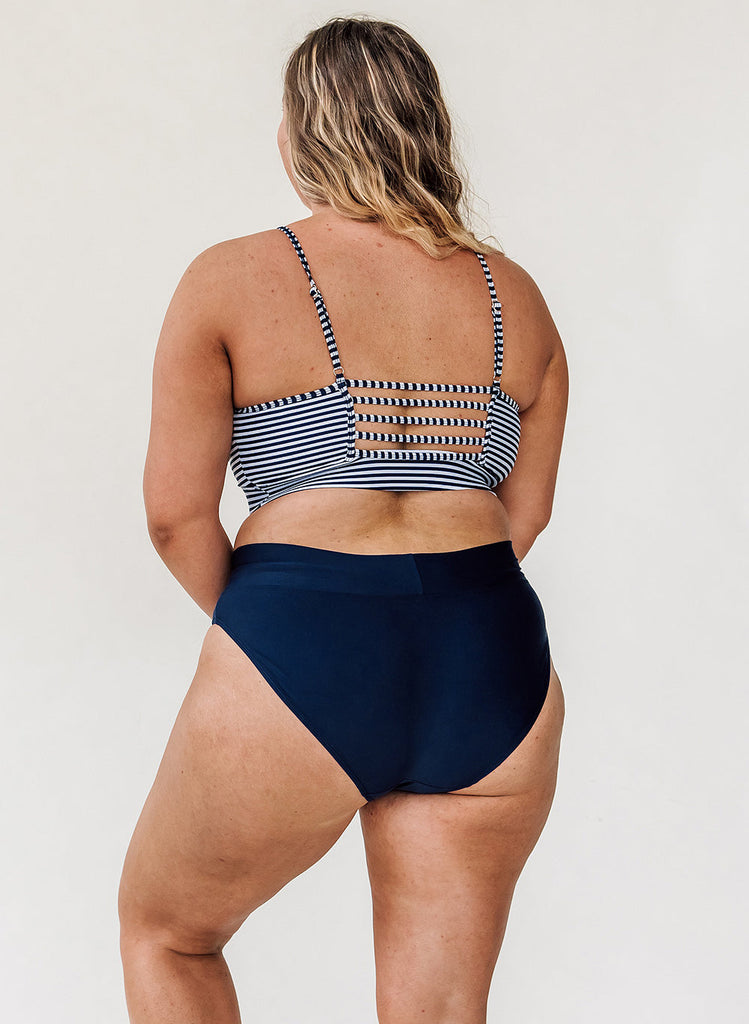 Photo of woman with her back facing us wearing a blue and white striped cropped swim top with blue classic low rise swim bottoms