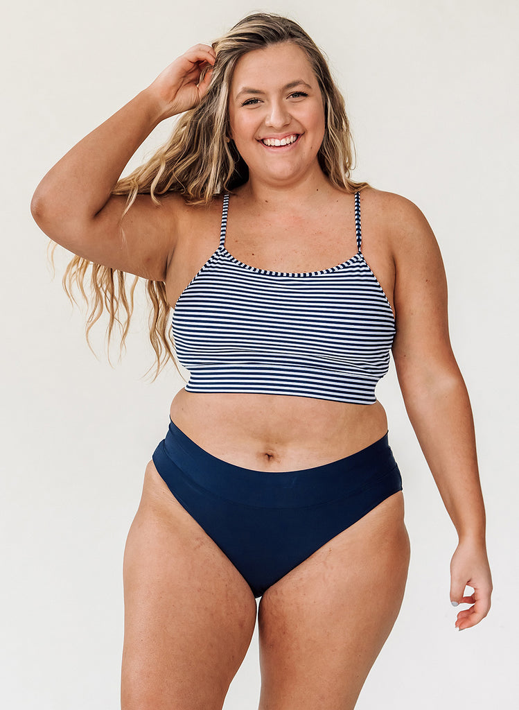 Photo of a woman wearing a blue and white striped cropped swim top with blue classic low rise swim bottoms