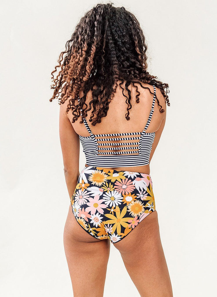 Photo of a woman wearing a black and white stripe swim bralette and a multi color floral swim bottom- back angle