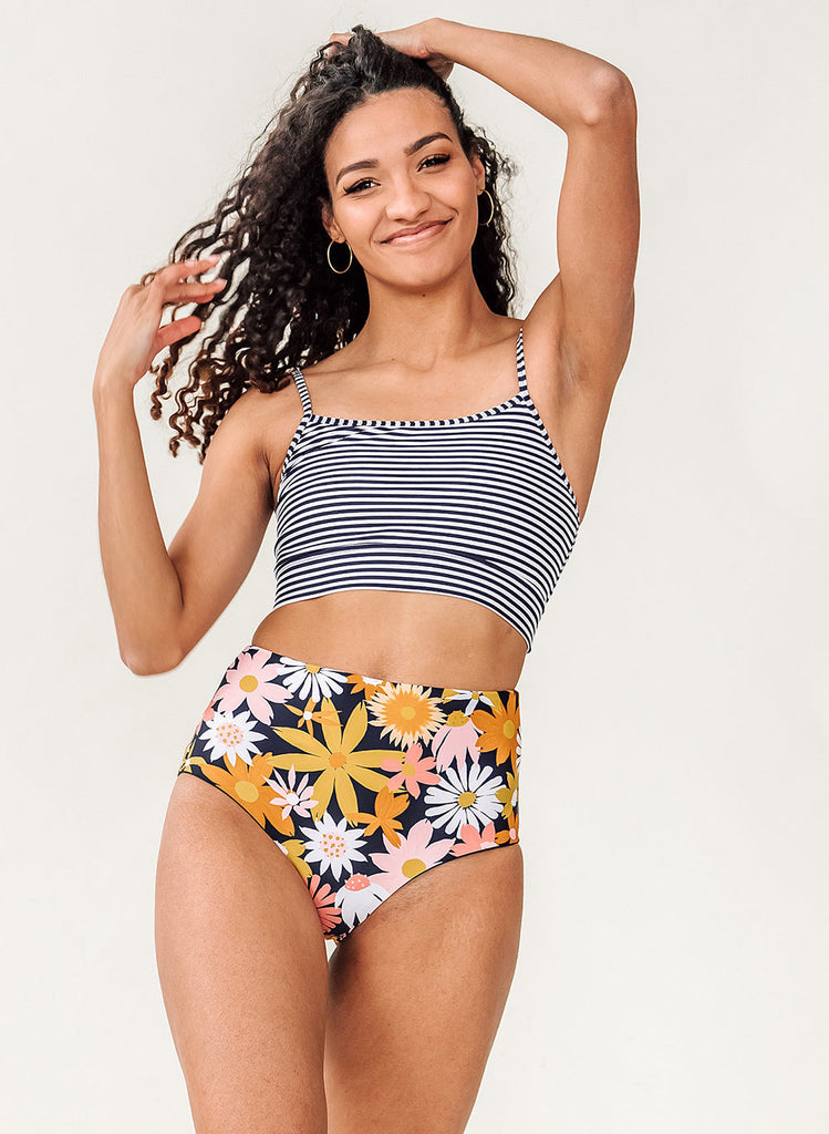 Photo of a woman wearing a blue and white striped cropped swim top with yellow and pink floral high waist swim bottoms