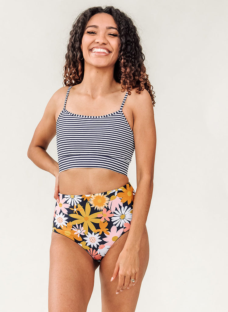 Photo of woman posing with her hand on her hip while wearing a blue and white striped cropped swim top with yellow and pink floral high waist swim bottoms