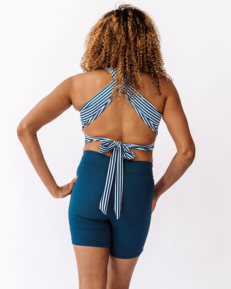 Photo of a woman wearing an Indigo stripe cross-back swim crop top and an Indigo bike short swim bottom back angle
