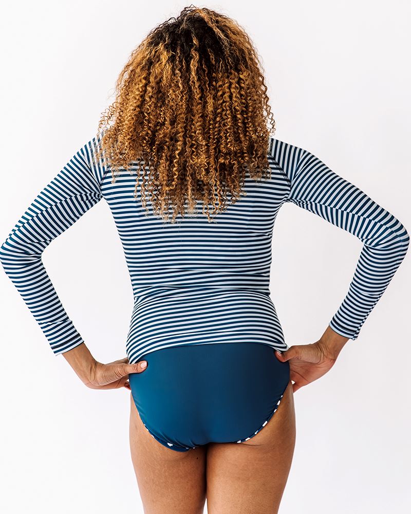Photo of a woman wearing an Indigo stripe rash guard swim top and an Indigo swim bottom back angle