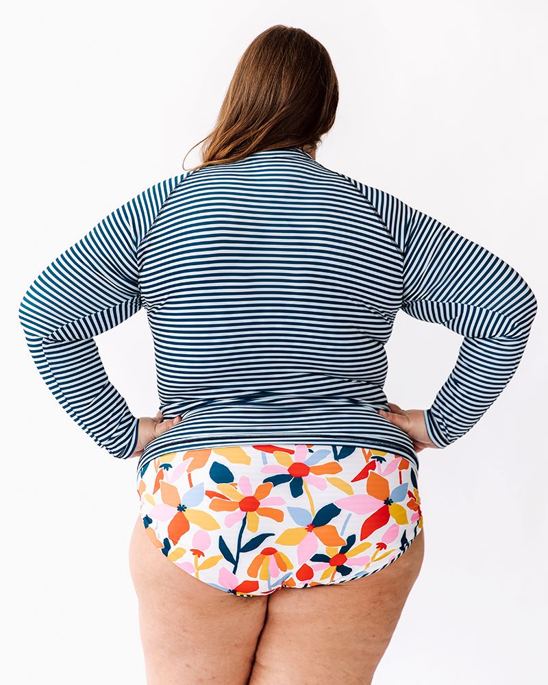 Photo of a woman wearing an Indigo stripe rash guard swim top and a multi color swim bottom back angle