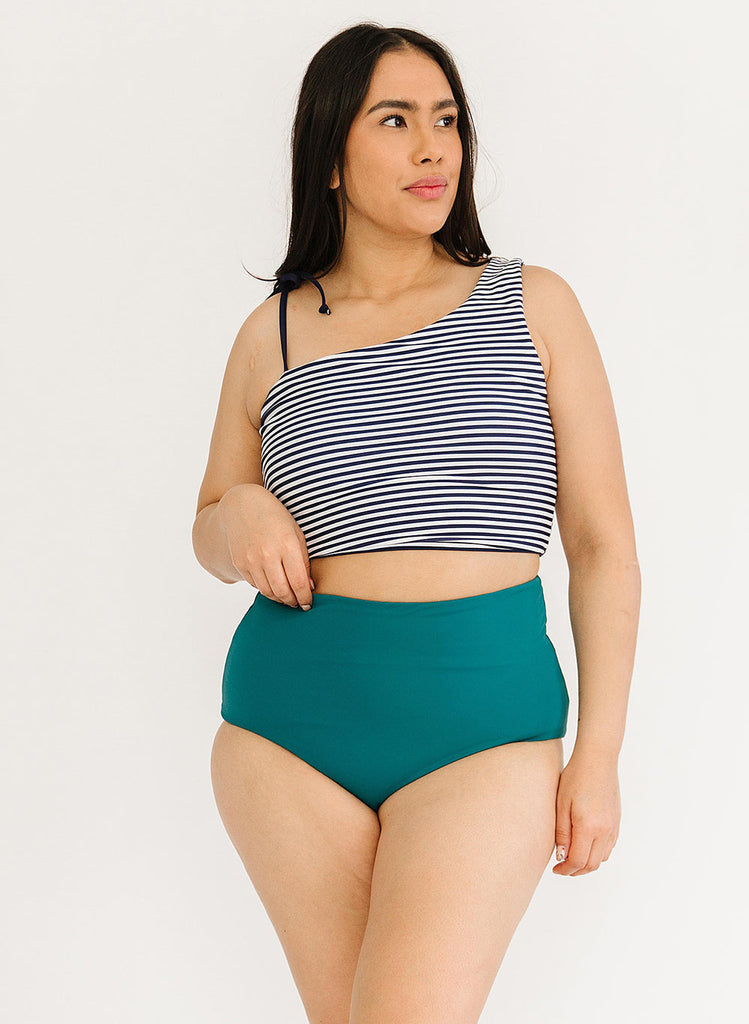 Photo of a woman wearing a striped one-shoulder swim crop top and a dark green swim bottom