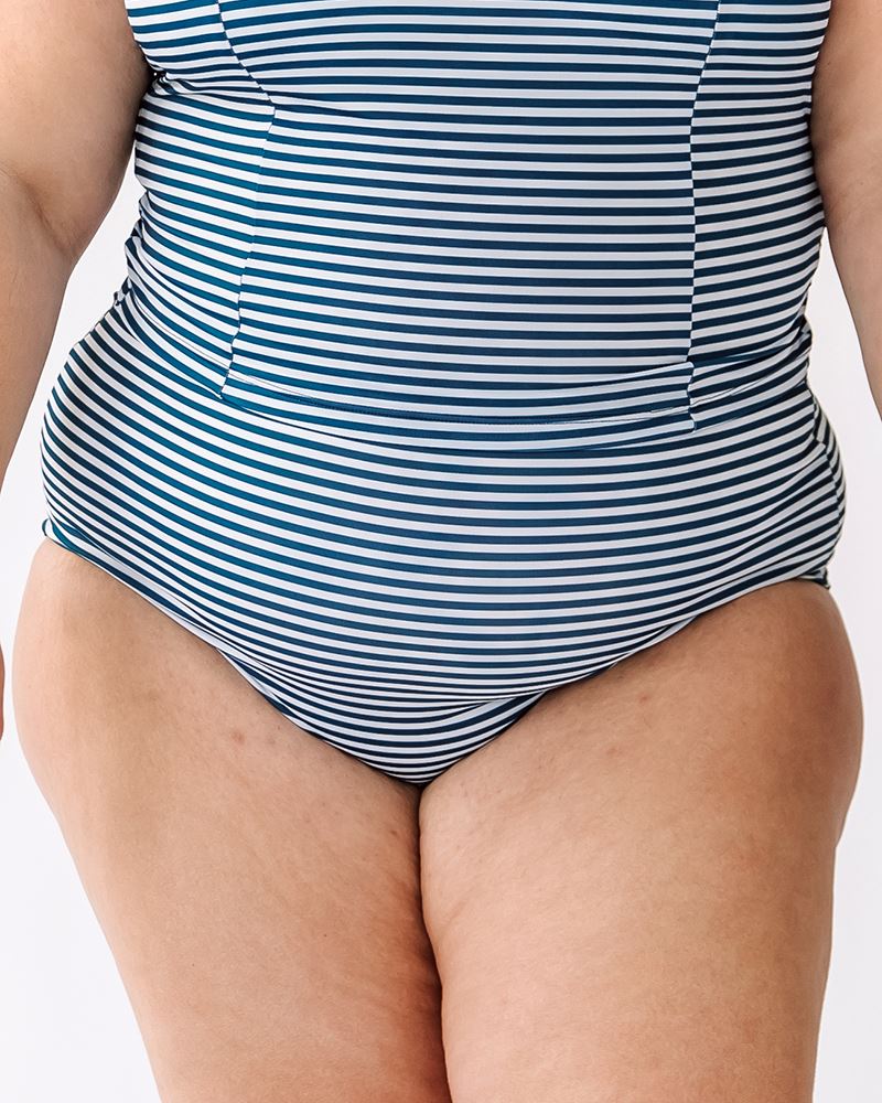 Photo of a woman wearing a June floral/ Indigo stripe reversible swim bottom Indigo stripe side and and Indigo stripe swim crop top