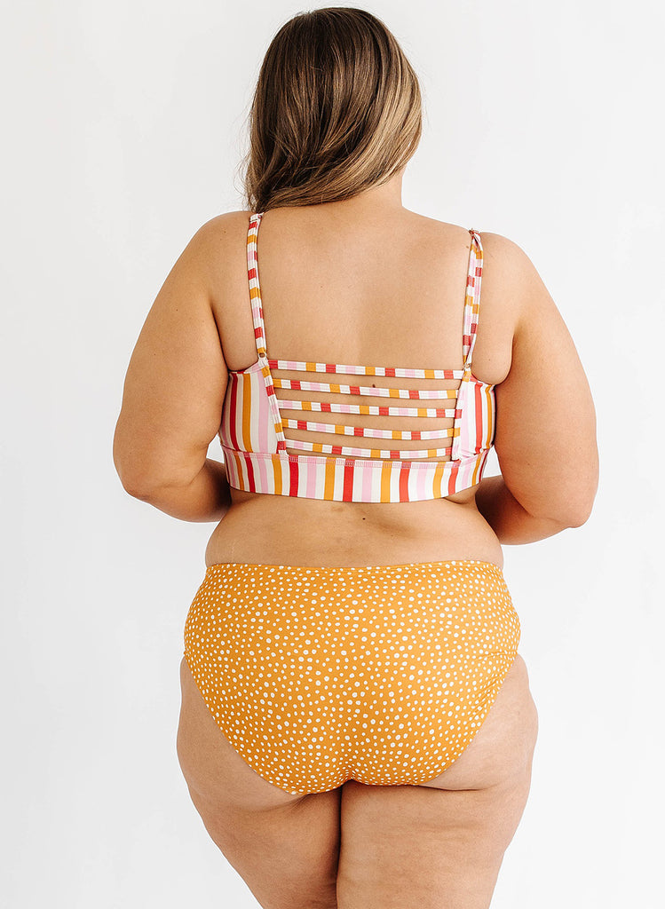 Photo of woman multi color stripe bralette swim top with orange and white dot mid waist swim bottoms back angle