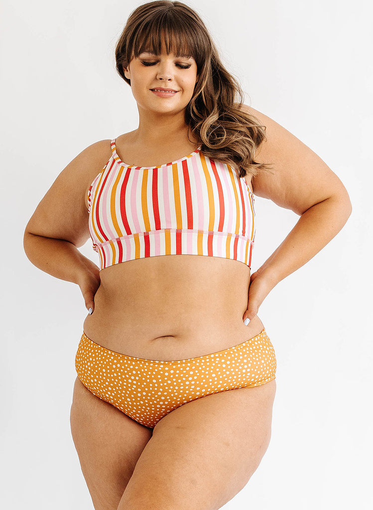Photo of woman wearing multi color stripe bralette swim top with orange and white dot swim bottoms