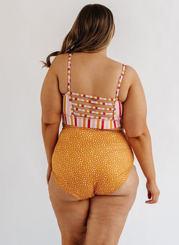 Photo of woman wearing multi color stripe bralette swim top with orange and white dot swim bottoms back angle