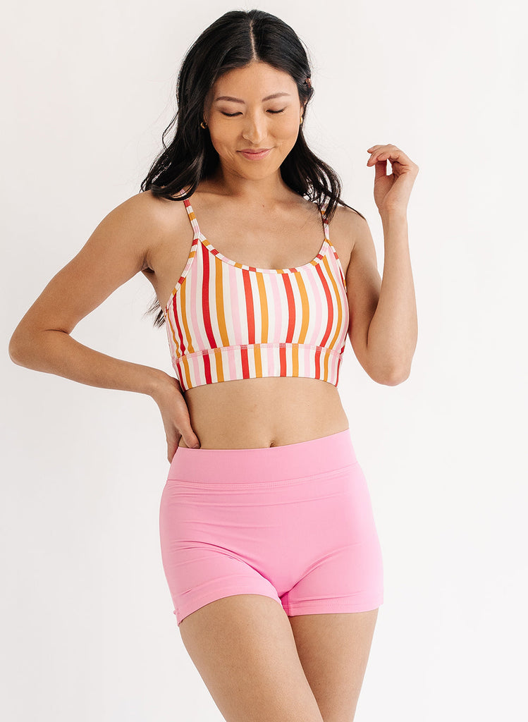 Photo of woman wearing multi color stripe bralette swim top with pink swim shorts