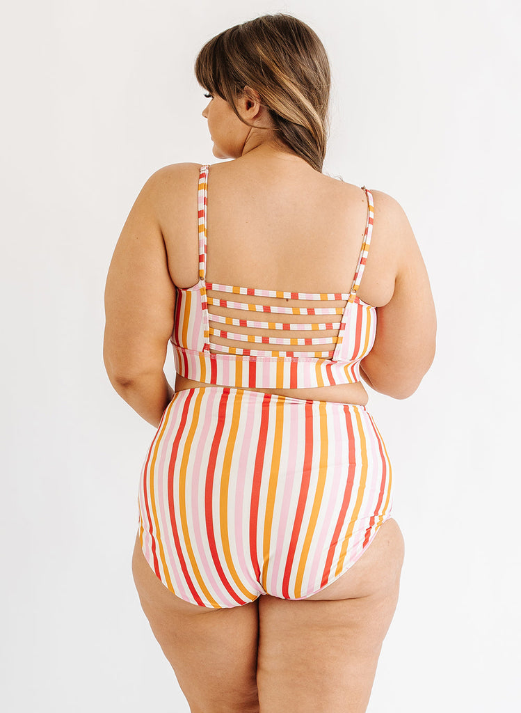 Photo of woman wearing multi color stripe bralette swim top with multi color stripe swim bottoms back angle