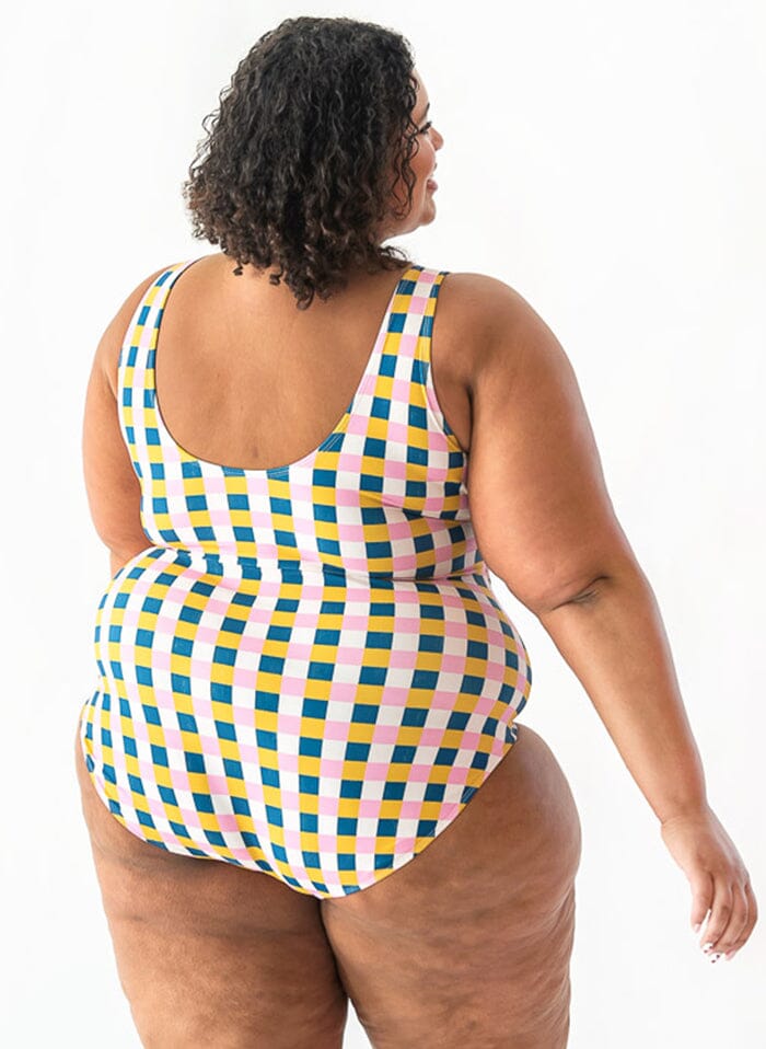 Photo of a woman with her back facing us wearing a multi colored checkered one piece swimsuit