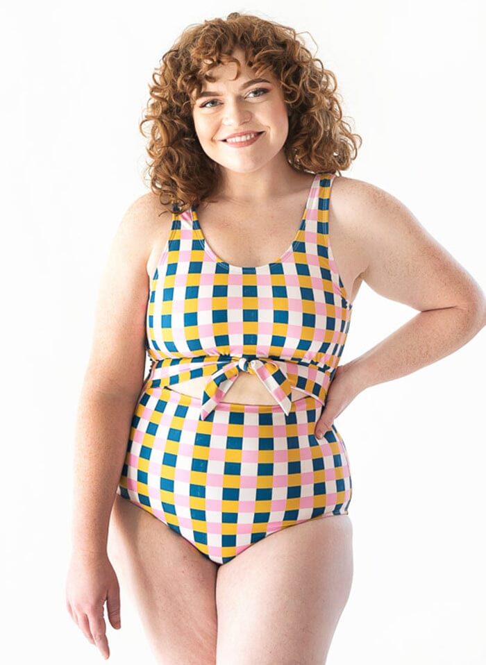 Photo of a woman with her hand on her hip wearing a multi colored checkered one piece swimsuit