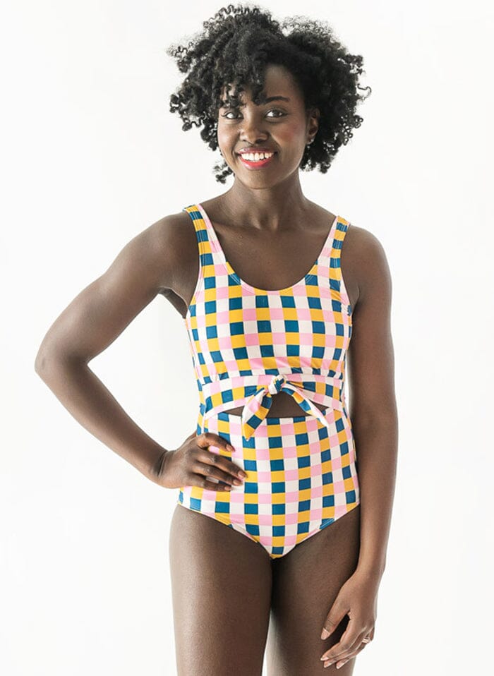 Photo of woman with her hand on her hip wearing a multi colored checkered one piece swimsuit