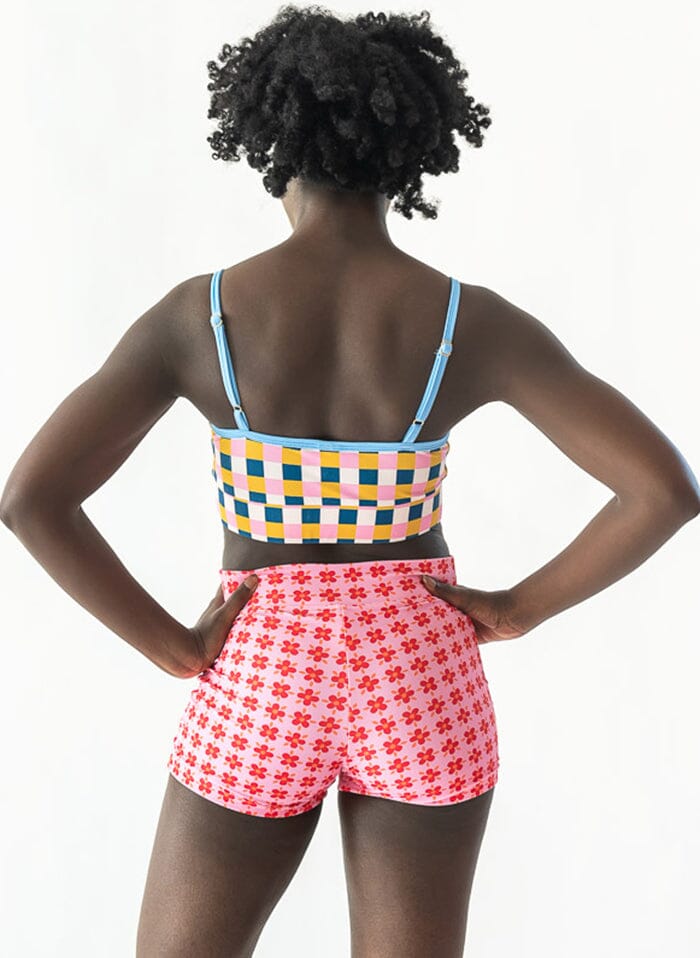 Photo of a woman wearing a pink Margrethe swim short bottom and a multi color checkered swim bralette back angle