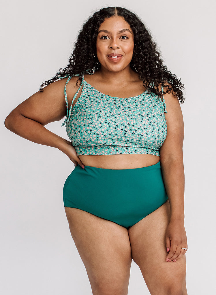 Photo of a woman wearing a green floral shoulder-tie swim crop top and a dark green swim bottom