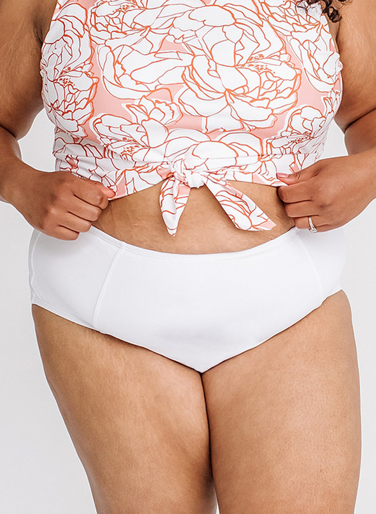 Close up photo of a woman wearing a pink and white floral cropped swim top with white high waist swim bottoms