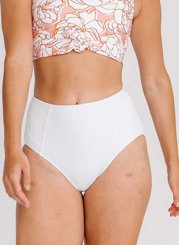 Close up photo of woman wearing a pink and white floral cropped swim top with white high waist swim bottoms