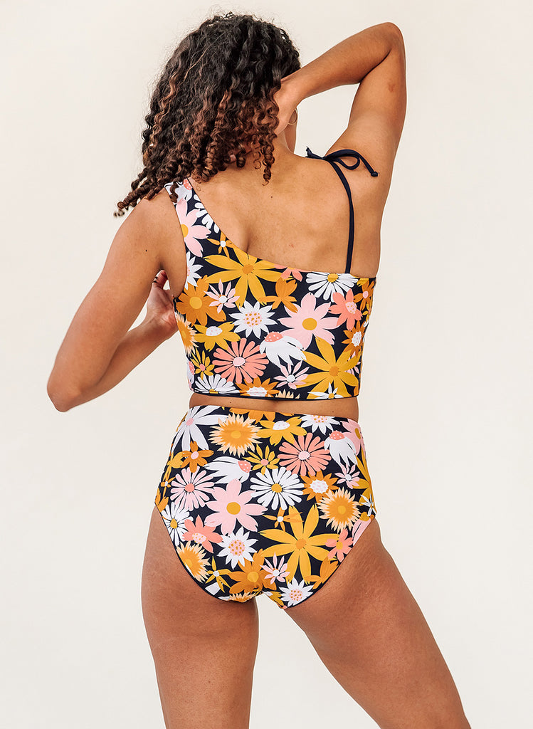 Photo of woman with her back facing us wearing a pink and yellow floral cropped swim top with pink and yellow floral high waist swim bottoms