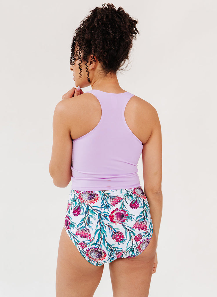Photo of a woman wearing a lavender swim crop top and a desert floral swim bottom- back angle
